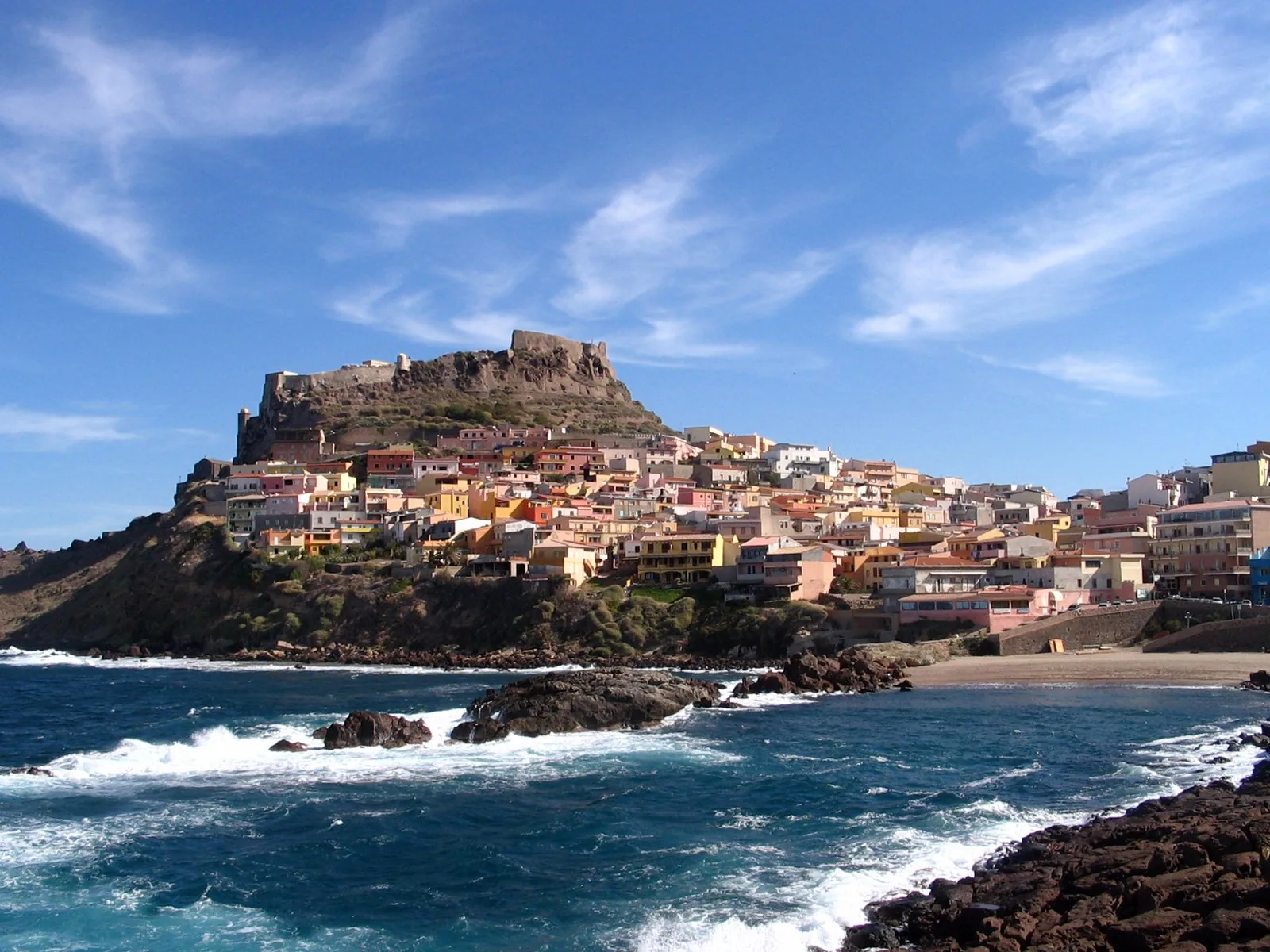 Il borgo di Castelsardo con le case colorate che salgono verso il castello sulla cima del promontorio, visto dagli scogli sul mare