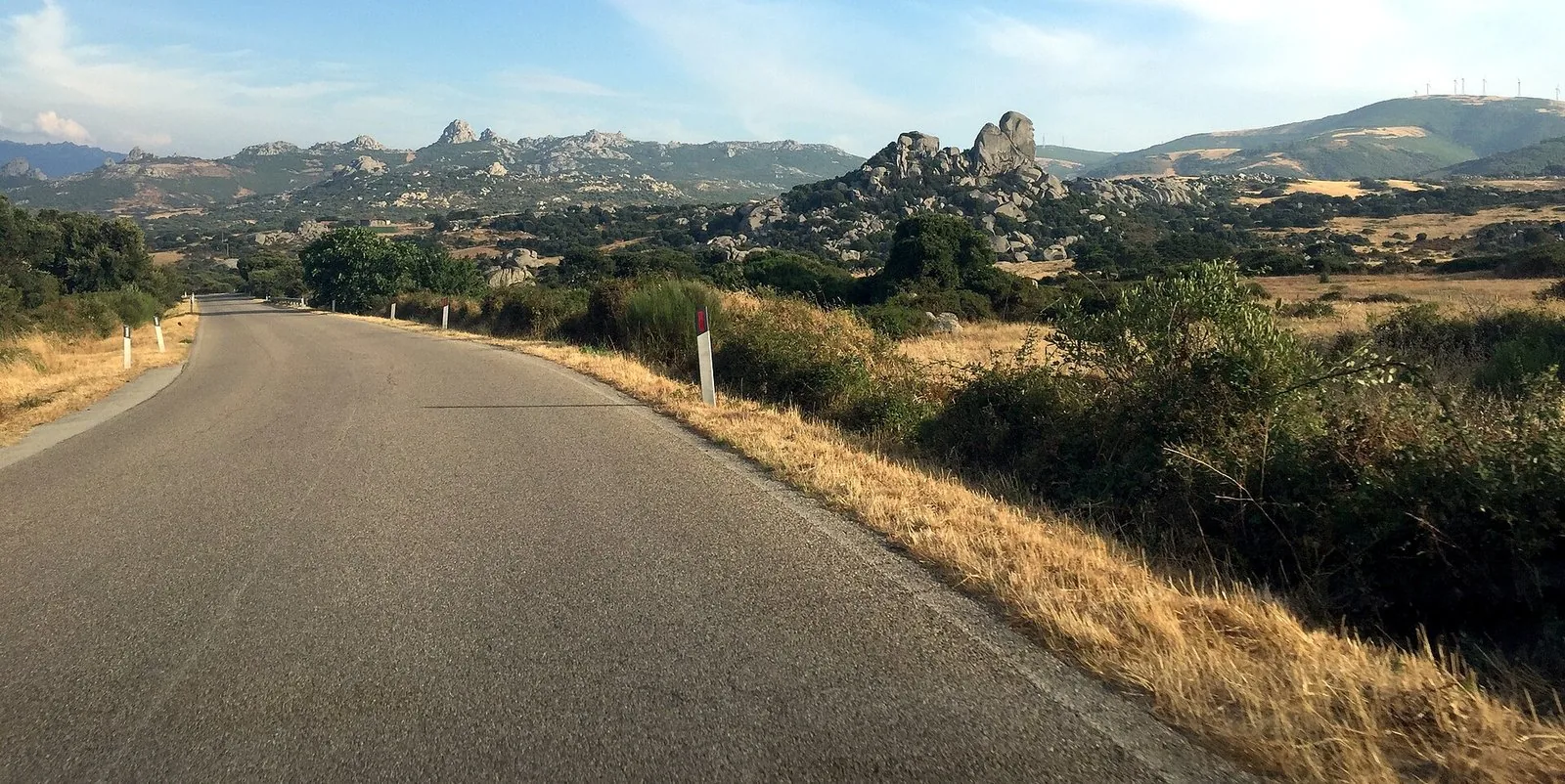 Strada asfaltata nell'entroterra della Gallura tra erba secca, macchia mediterranea e rilievi di granito